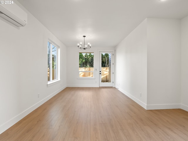 unfurnished room with an inviting chandelier, a wall mounted AC, and light wood-type flooring