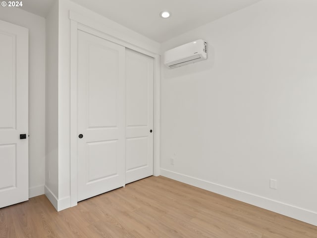 unfurnished bedroom featuring a closet, a wall mounted AC, and light hardwood / wood-style flooring