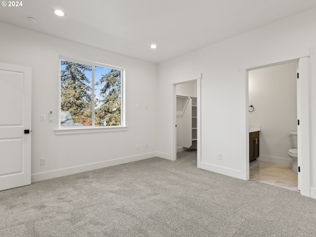 unfurnished bedroom featuring a closet, a spacious closet, light colored carpet, and ensuite bathroom