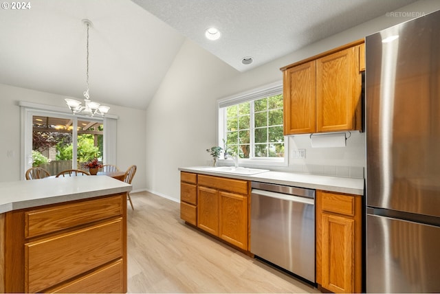 kitchen with lofted ceiling, appliances with stainless steel finishes, plenty of natural light, and a chandelier