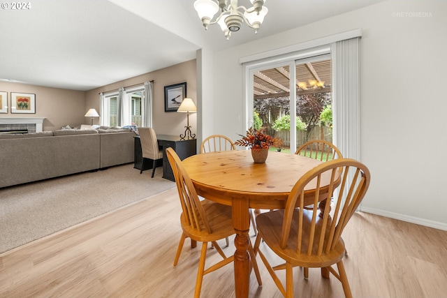 dining room with a tiled fireplace, light hardwood / wood-style floors, a chandelier, and plenty of natural light