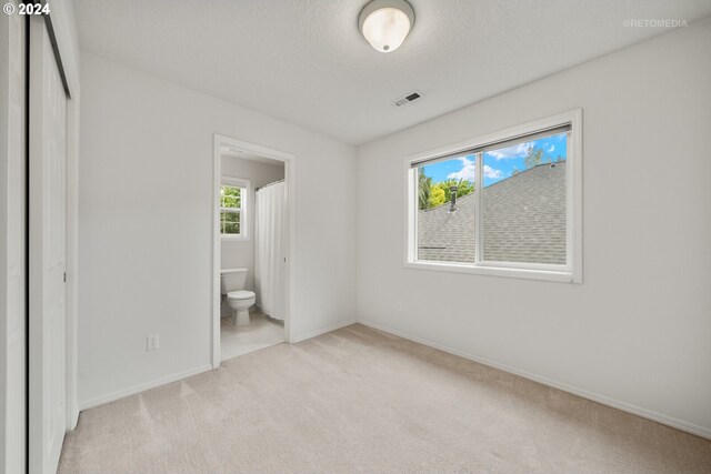 unfurnished bedroom featuring light carpet, connected bathroom, and a textured ceiling