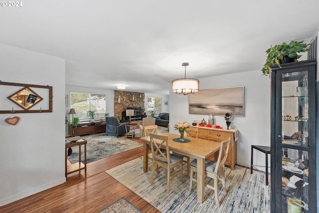 dining space with hardwood / wood-style floors, a chandelier, and a stone fireplace