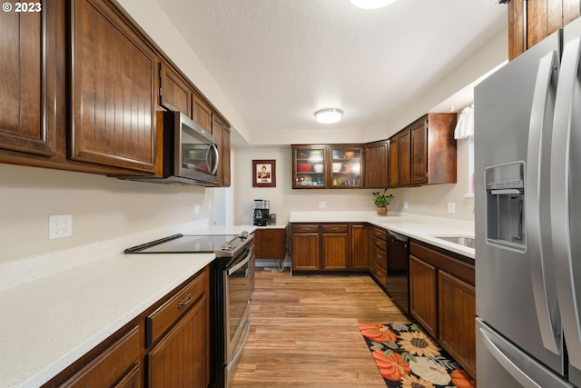 kitchen with appliances with stainless steel finishes, light wood-type flooring, sink, and a textured ceiling