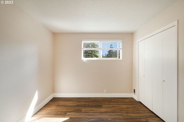 unfurnished bedroom with dark wood-type flooring, a closet, and a textured ceiling