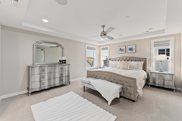 bedroom featuring light carpet, a raised ceiling, and baseboards