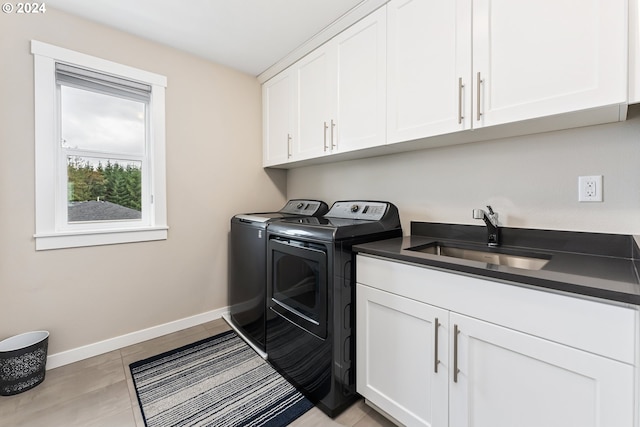 washroom featuring washing machine and clothes dryer, a sink, cabinet space, and baseboards