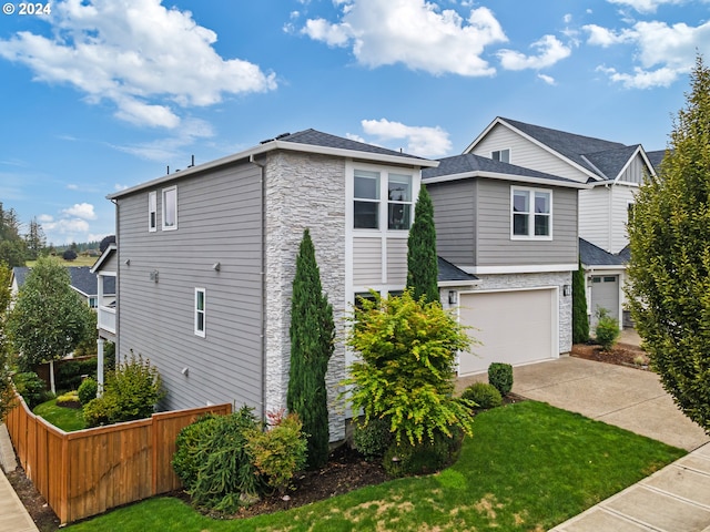 view of front of property featuring an attached garage, fence, stone siding, driveway, and a front lawn