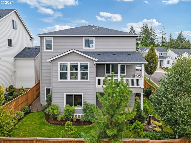 rear view of property featuring a balcony, a fenced backyard, a shingled roof, and a yard