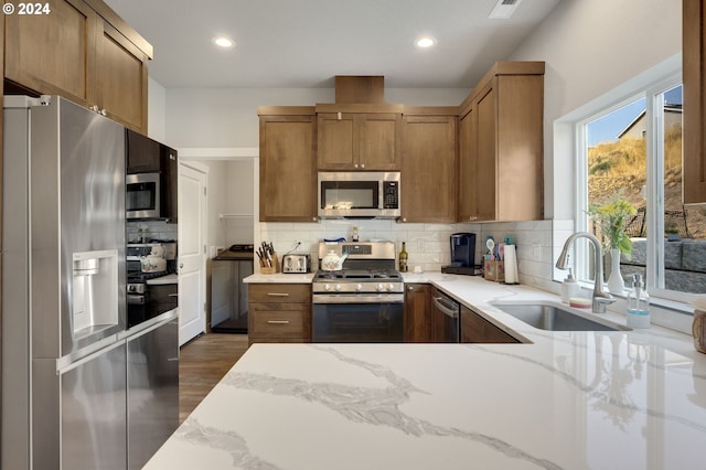 kitchen with sink, dark wood-type flooring, light stone counters, decorative backsplash, and appliances with stainless steel finishes