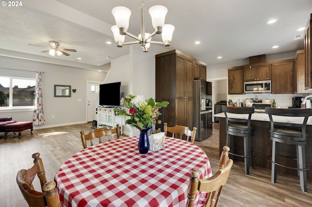 dining space with ceiling fan with notable chandelier and light hardwood / wood-style floors