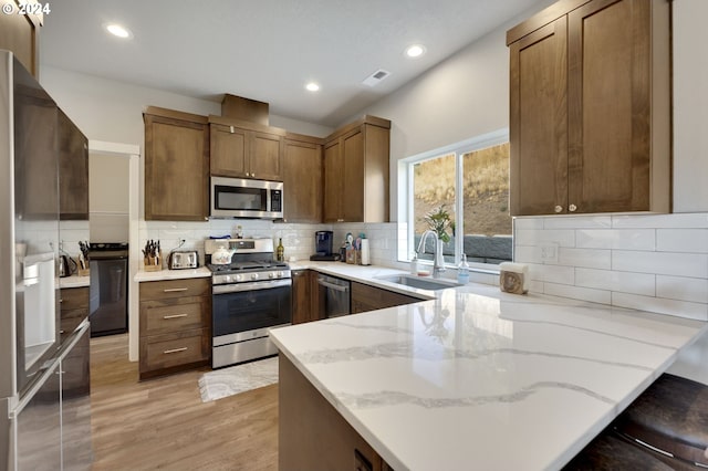 kitchen featuring kitchen peninsula, appliances with stainless steel finishes, light wood-type flooring, a kitchen bar, and sink