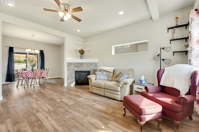 living room with ceiling fan with notable chandelier, beam ceiling, a tiled fireplace, and light hardwood / wood-style flooring