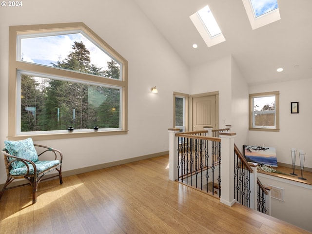 living area featuring a skylight, high vaulted ceiling, and light wood-type flooring