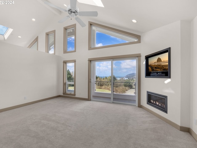 unfurnished living room with a skylight, high vaulted ceiling, ceiling fan, and light carpet