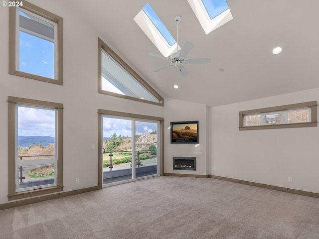 unfurnished living room featuring a skylight, high vaulted ceiling, light carpet, and ceiling fan