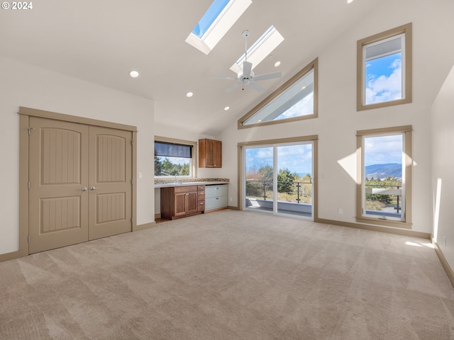 unfurnished living room with a skylight, light colored carpet, ceiling fan, and high vaulted ceiling