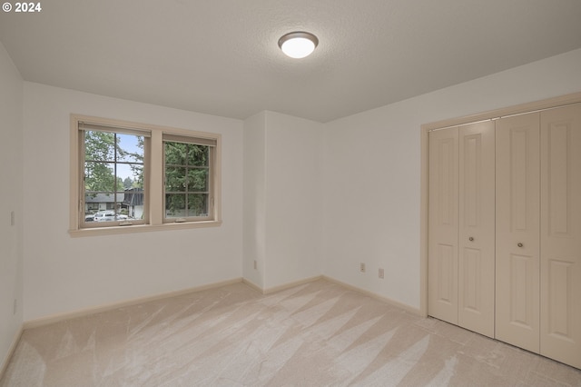 unfurnished bedroom featuring a closet, light colored carpet, and a textured ceiling