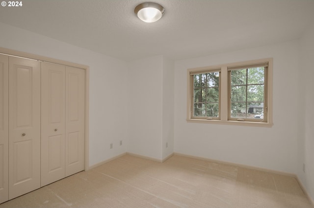 unfurnished bedroom featuring light colored carpet, a textured ceiling, and a closet