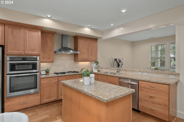 kitchen featuring wall chimney exhaust hood, sink, kitchen peninsula, light hardwood / wood-style flooring, and appliances with stainless steel finishes