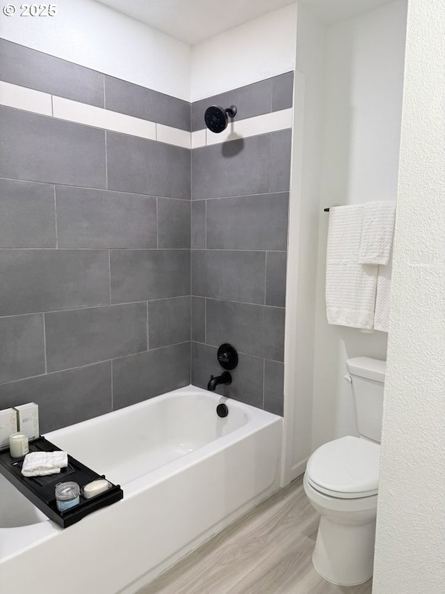 bathroom with tiled shower / bath combo, toilet, and wood-type flooring