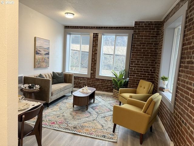 sitting room with brick wall, a textured ceiling, and hardwood / wood-style flooring