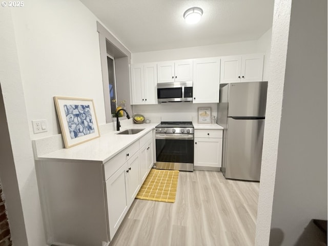 kitchen featuring appliances with stainless steel finishes, a textured ceiling, sink, light hardwood / wood-style flooring, and white cabinets