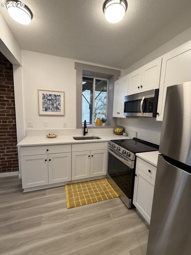 kitchen with white cabinetry, sink, stainless steel appliances, and light wood-type flooring