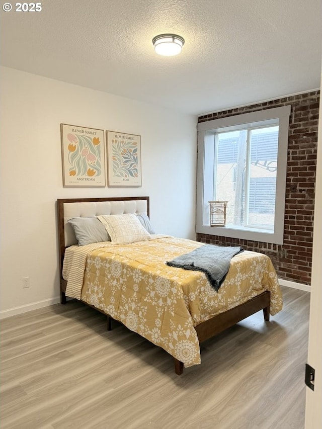 bedroom with wood-type flooring, a textured ceiling, and brick wall