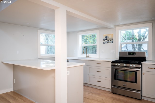 kitchen featuring white cabinets, light hardwood / wood-style floors, stainless steel range with gas stovetop, and plenty of natural light