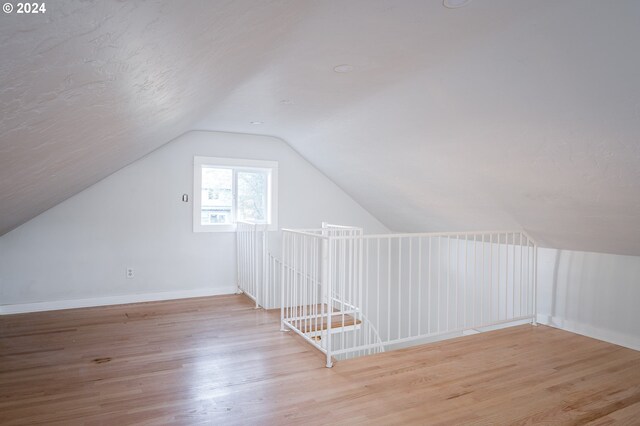 additional living space with light wood-type flooring and vaulted ceiling