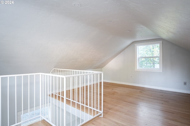 additional living space with hardwood / wood-style floors, a textured ceiling, and lofted ceiling