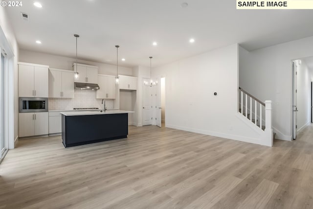 kitchen with stainless steel appliances, a kitchen island with sink, light hardwood / wood-style floors, white cabinetry, and hanging light fixtures