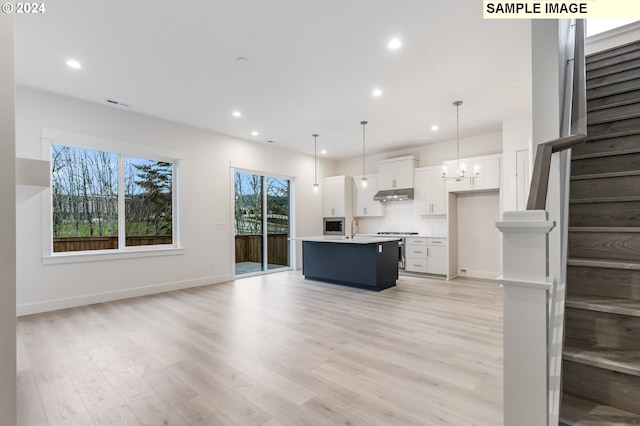 kitchen featuring white cabinets, a center island with sink, decorative backsplash, decorative light fixtures, and light hardwood / wood-style floors