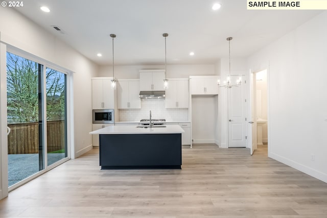 kitchen featuring white cabinets, light hardwood / wood-style floors, stainless steel microwave, and an island with sink