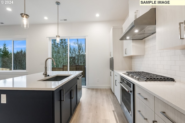 kitchen with sink, stainless steel appliances, an island with sink, extractor fan, and decorative light fixtures