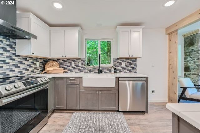 kitchen featuring white cabinetry, wall chimney exhaust hood, gray cabinets, appliances with stainless steel finishes, and light wood-type flooring