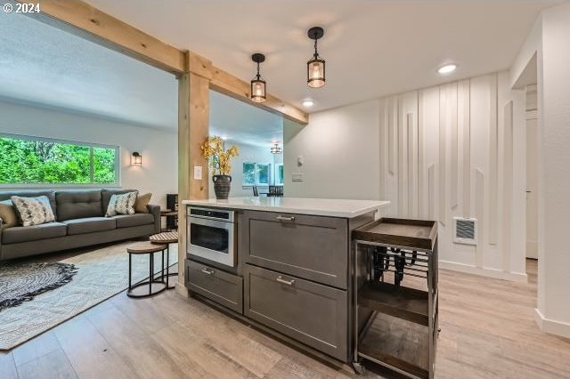 kitchen featuring gray cabinetry, stainless steel oven, hanging light fixtures, light hardwood / wood-style flooring, and beverage cooler