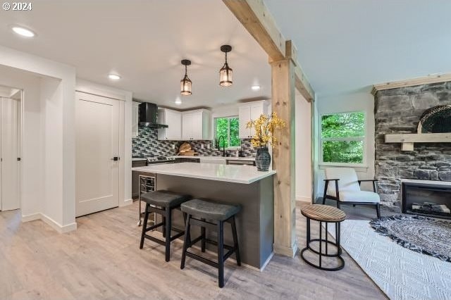 kitchen with a kitchen bar, light wood-type flooring, wall chimney exhaust hood, decorative light fixtures, and white cabinetry