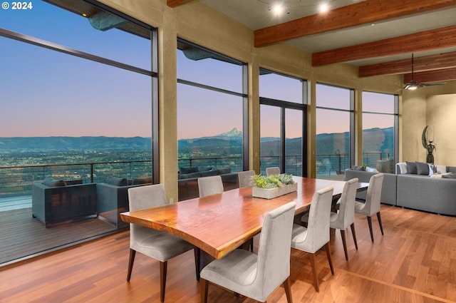 dining area with a healthy amount of sunlight, a mountain view, beamed ceiling, and light hardwood / wood-style floors