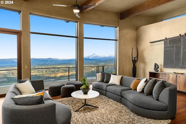 living room featuring a mountain view, ceiling fan, a barn door, beamed ceiling, and dark hardwood / wood-style flooring