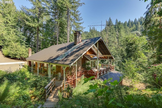 view of front facade with covered porch, a wooded view, and a chimney