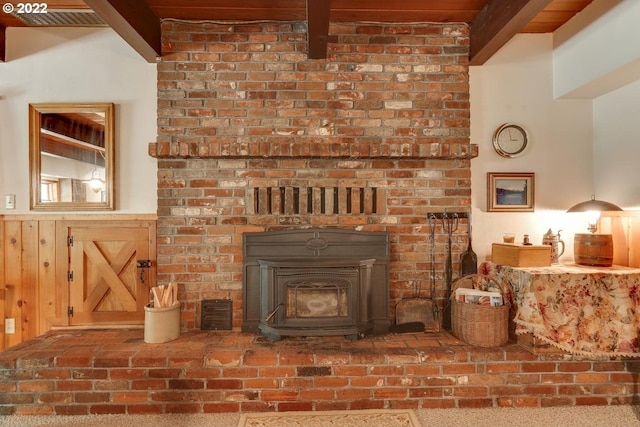 room details featuring carpet flooring, beam ceiling, a wood stove, and a brick fireplace