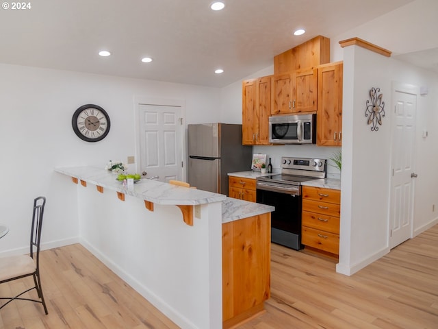 kitchen with a breakfast bar area, light hardwood / wood-style floors, kitchen peninsula, and appliances with stainless steel finishes