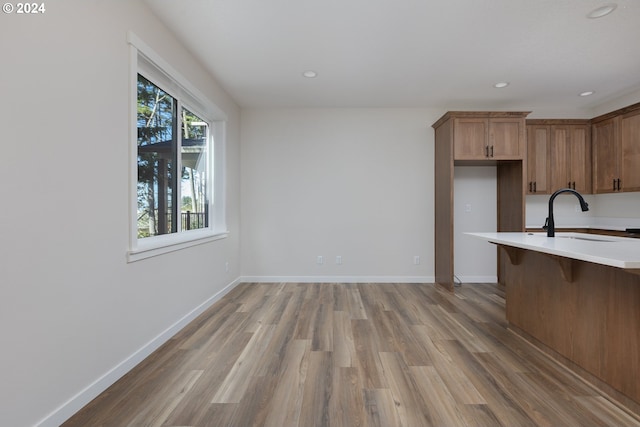 kitchen with light countertops, a breakfast bar area, baseboards, a sink, and wood finished floors