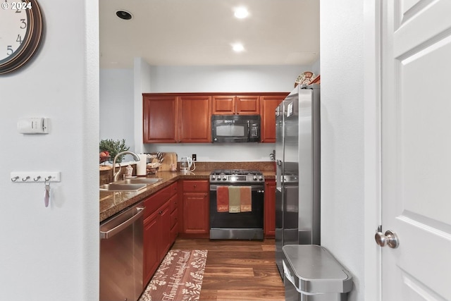 kitchen featuring appliances with stainless steel finishes, dark hardwood / wood-style floors, dark stone countertops, and sink