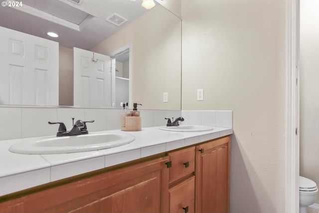 full bathroom with toilet, double vanity, a sink, and visible vents