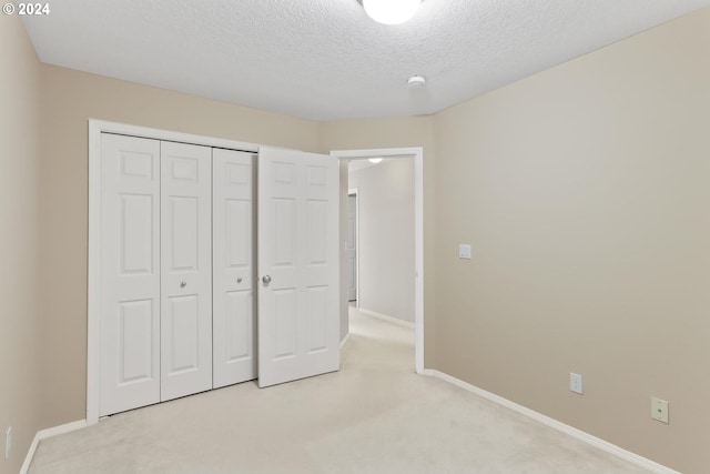 unfurnished bedroom featuring a closet, a textured ceiling, and light colored carpet