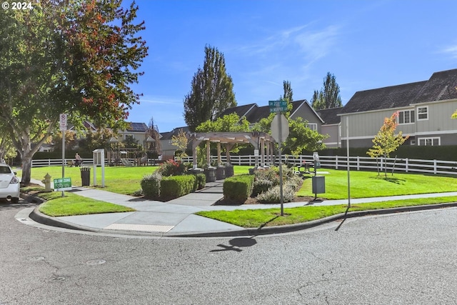 view of community featuring fence, a residential view, a lawn, and a pergola