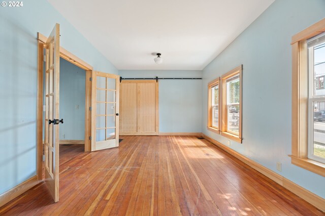 unfurnished bedroom with a barn door, light hardwood / wood-style flooring, and french doors